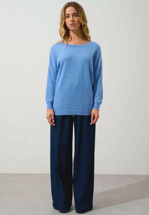 Hellblauer Pullover aus weichem Material mit lockerer Passform, Rundhalsausschnitt und langen Ärmeln, kombiniert mit weit geschnittenen, dunklen Jeanshosen.