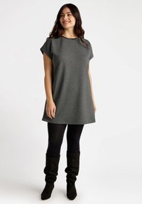 Graues kurzärmliges Kleid mit leicht ausgestellter A-Linie, ausgestattet mit einem runden Ausschnitt, der mit schwarzen Akzenten verziert ist, kombiniert mit schwarzen Strumpfhosen und knielangen Stiefeln.