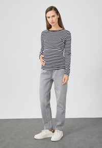 Long-sleeve black and white striped shirt paired with gray jeans and white sneakers. The shirt features a round neckline and fitted sleeves.
