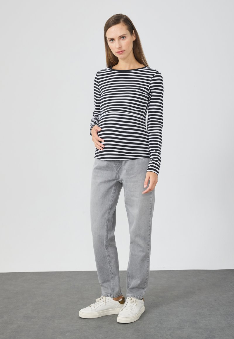 Long-sleeve black and white striped shirt paired with gray jeans and white sneakers. The shirt features a round neckline and fitted sleeves.