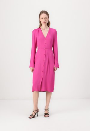 Fuksia midi mekko, jossa on pitkät hihat, V-pääntie, napituskiristys ja vyöllä solmittava nauha. Yhdistetty mustiin korsettikenkiin.