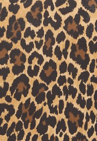 Tkanina s leopardím vzorem s béžovým pozadím a velkými černými a hnědými skvrnami, které zobrazují různorodé tvary a textury po celém povrchu.