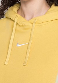 Felpa con cappuccio gialla con una texture morbida, caratterizzata da un cappuccio con coulisse e un piccolo logo Nike bianco sulla zona del petto.