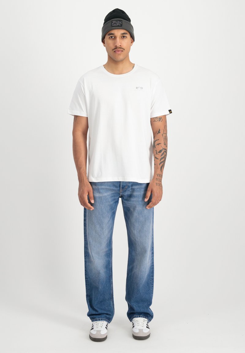 Hvid bomulds t-shirt med et lille logo, parret med lyseblå lige ben jeans. Båret med en sort og grå beanie. Hvide sneakers.
