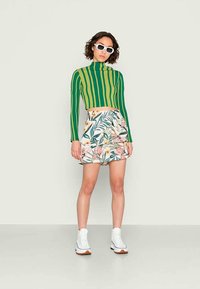 Sweater cropped de manga longa com riscas verdes e amarelas, combinado com uma saia estampada de flores com folhas rosas e verdes, usado com ténis brancos.
