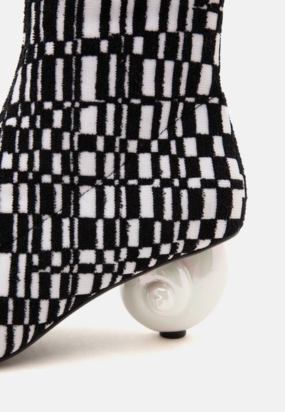 Chaussure à motif géométrique noir et blanc avec un talon rond blanc en forme de spirale distinctif sur un fond clair.