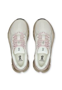 Een paar crème kleurige hardloopschoenen met roze veters en beige zolen, merk "On Cloudrunner," van bovenaf bekeken op een witte achtergrond.