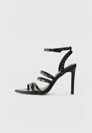 Mustad mustakotid sandaalid mitme läikiva rihmaga, pahkluude külge kinnitamisega ja ruudukujulise varbaga. Sile nahk, terav konts.