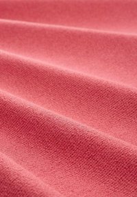 Strukturstoff in einem sanften Rosaton, mit einer glatten Oberfläche und sanften Falten, die ein einheitliches Muster und eine gleichmäßige Farbe zeigen.