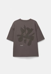 Grå oversized t-shirt med korte ærmer, der har et stort mørkt trykdesign på ryggen og en lille tekstdetalje nær kanten.