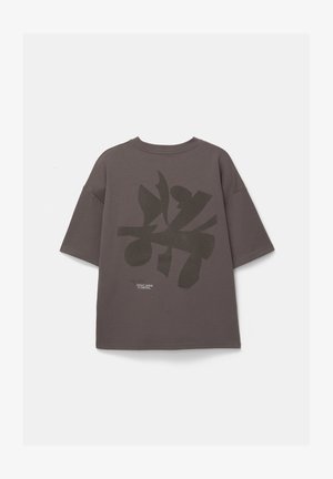 Graues oversized T-Shirt mit kurzen Ärmeln, das ein großes dunkles Druckdesign auf dem Rücken und ein kleines Textdetail nahe dem Saum aufweist.