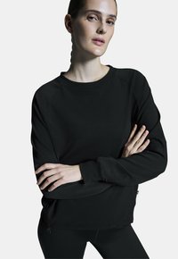 Fekete pulóver, kerek nyakkal, hosszú raglánujjakkal, bordás mandzsettával, laza szabással, fekete leggingsszel párosítva.