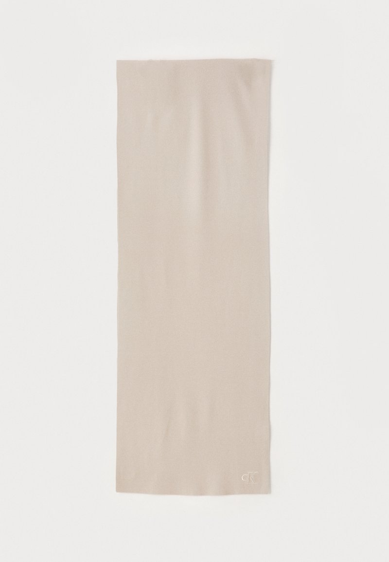 Beige sall, mis pehme materjal on sileda tekstuuriga ja ristkülikukujuline. Alumises nurgas on diskreetne logo.