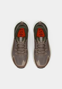 Pruunid spordijalatsid hingava võrgukangaga pealiskihi, tumeroheliste detailide ja paksu valge vahetallaga. Omavad robustsemat siluetti ja tekstuurseid detaile.