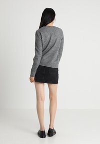 Szary sweter dzianinowy z okrągłym dekoltem, połączony z czarną dżinsową mini spódnicą z postrzępionym dołem. Całość uzupełniają czarne buty.