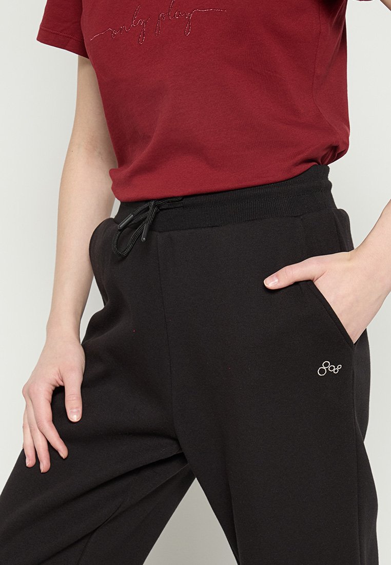 Pantalon de survêtement noir avec une taille élastique et un cordon de serrage. Il dispose de poches latérales et d'un petit logo blanc sur la jambe. Texture de tissu douce.