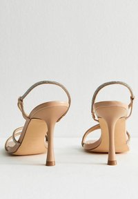 Nude högklackade sandaler med stilett design. Har delikata remmar prydda med små rhinstenar. Slät läderstruktur.