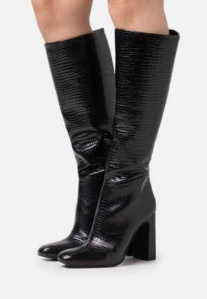Bottes noires brillantes montantes en cuir crocodile, avec un bout pointu et un talon épais. Matériau lisse et design ajusté.