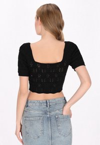 Czarny dziergany crop top z krótkimi rękawami w stylu puff i kwadratowym tyłem, zdobiony delikatnym wzorem koronkowym. Noszony z jasnoniebieską spódnicą dżinsową.