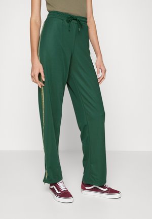 Calças de desporto verdes com um corte relaxado, cintura com cordão e detalhe de riscas verticais contrastantes. Feitas de um material suave e texturado.