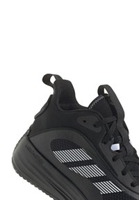 Chaussure de sport noire avec un dessus en maille au motif de rayures blanches, semelle en caoutchouc et languette à l'arrière pour un enfilage facile.