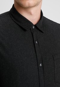 Zwart overhemd met knopen, gemaakt van gestructureerde stof, voorzien van een kraag, een borstzak en grijze knopen in een strak design.