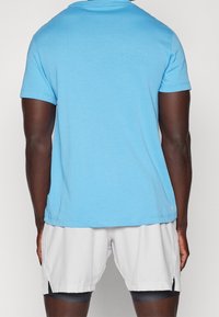 Man wearing light blue short-sleeve t-shirt and white athletic shorts with black compression shorts underneath, shown from the back.