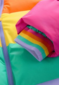 Kleurrijke pufferjack met levendige roze, oranje, gele en groene panelen, met een regenbooggestreepte manchet die eruit steekt.