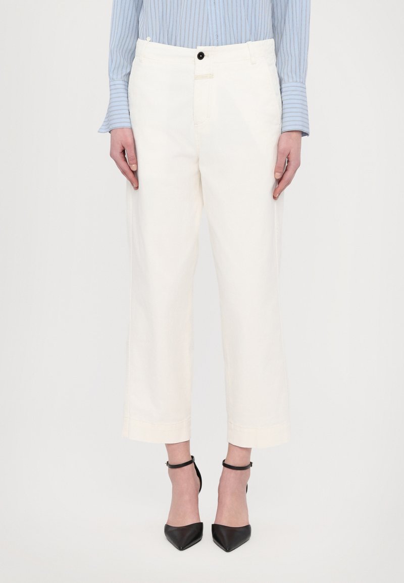 White wide-leg trousers with a button closure, belt loops, and hemmed cuffs, paired with black pointed heels and a light blue striped shirt.