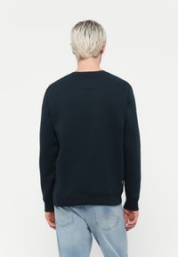 Felpa blu navy con scollatura rotonda e polsini a costine, realizzata in un materiale morbido. Presenta un piccolo etichetta sull'orlo.