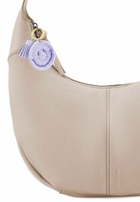 Borsa a spalla in pelle beige con design curvo, chiusura con zip, dettagli cuciti e un charm decorativo a forma di sorriso ricamato in viola.