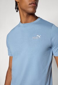 Lyseblå t-skjorte i myk stoff med rund hals og korte ermer. Fronten har en brodert hvit Puma-logo.