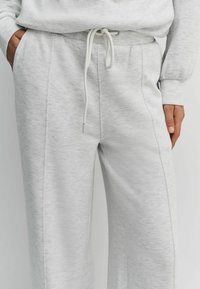 Light gray sweatpants made of soft fabric, featuring a drawstring waist, side pockets, and a relaxed fit with visible stitching details.