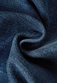 Närbild av mörkblå denimtyg med synligt vävmönster vikt i mjuka kurvor och skuggor.