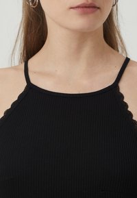 Black ribbed tank top featuring slim straps with lace detailing along the neckline. Soft texture with a fitted design.