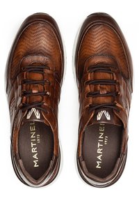 Zapatillas de cuero marrón con detalles perforados, puntera redonda, cierre con cordones y suelas blancas; cuenta con un logo en la lengüeta y acentos texturizados.