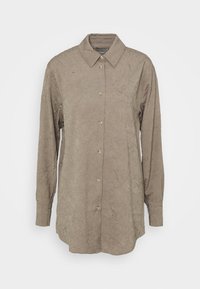 Camicia abbottonata in un tessuto marrone chiaro e sgualcito. Presenta un colletto classico, maniche lunghe e cinque bottoni dorati lungo la parte anteriore.