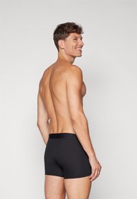 Black boxer briefs made from a smooth fabric, featuring a plain elastic waistband and a fitted design. Model shown from the side.