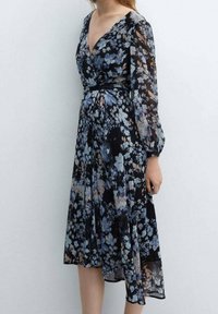 Kwiatowa, przezroczysta sukienka z głębokim dekoltem w kształcie litery V, długimi rękawami i ściągniętą w talii. Ciemna baza z niebieskimi i brzoskwiniowymi wzorami kwiatowymi. Sylwetka w kształcie litery A.