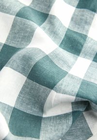 Tissu doux avec un motif à carreaux turquoise et blanc, présenté avec des plis doux et une texture visible.