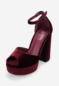 Sandalia de tacón alto de terciopelo burdeos con punta abierta, tira en el tobillo y tacón block, que presenta una textura suave y una plataforma en la parte delantera.
