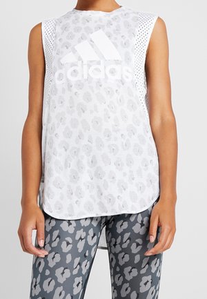 Person, die ein weißes ärmelloses Adidas-Oberteil mit grauem Leopardenmuster und passende Leggings mit grauem Leopardenmuster trägt.