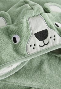 Grön frottéhandduk med huva, prydd med ett björnfacedesign. Mjuk textur med broderade detaljer för ögon, näsa och mun.