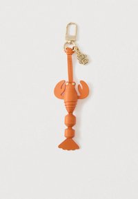 Oranž värvi homaarikujuline nahast võtmehoidja, millel on kuldne konks ja väike kuldne initsiaalidega ripats, valgel taustal.