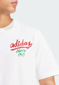 Hvid bomulds T-shirt med rød og grøn broderet tekst "adidas Since 1949." Klassisk crew neckline og korte ærmer.