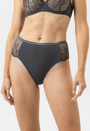 Femme portant un sous-vêtement taille haute gris foncé avec des panneaux latéraux transparents brodés de fleurs, assorti à un soutien-gorge coordonné.