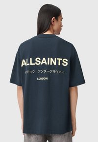 Μπλούζα από βαμβάκι σε ναυτικό μπλε χρώμα με μεγάλο λευκό κείμενο στην πίσω πλευρά: "ALLSAINTS", ιαπωνικοί χαρακτήρες και "LONDON" στο κάτω μέρος. Κοντά μανίκια.