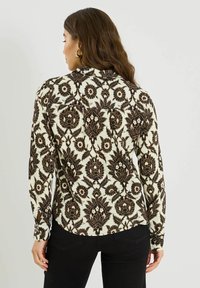 Blusa de manga larga con un estampado floral en negro y beige, con dobladillo redondeado y puños con botón, confeccionada en una tela suave.
