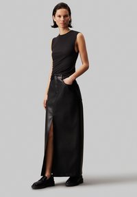 Top senza maniche nero abbinato a una lunga gonna in pelle nera con spacchi laterali e tasche, completato da mocassini neri chunky.