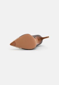 Chaussure à talon pointu en daim gris foncé avec un talon fin marron. La semelle est lisse avec un accent doré au bout.